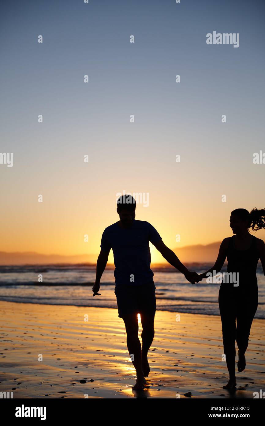 Beginnen Sie den Tag mit etwas Zweisamkeit. Silhouettenbild eines Paares, das beim Sonnenaufgang läuft und die Hände hält. Stockfoto