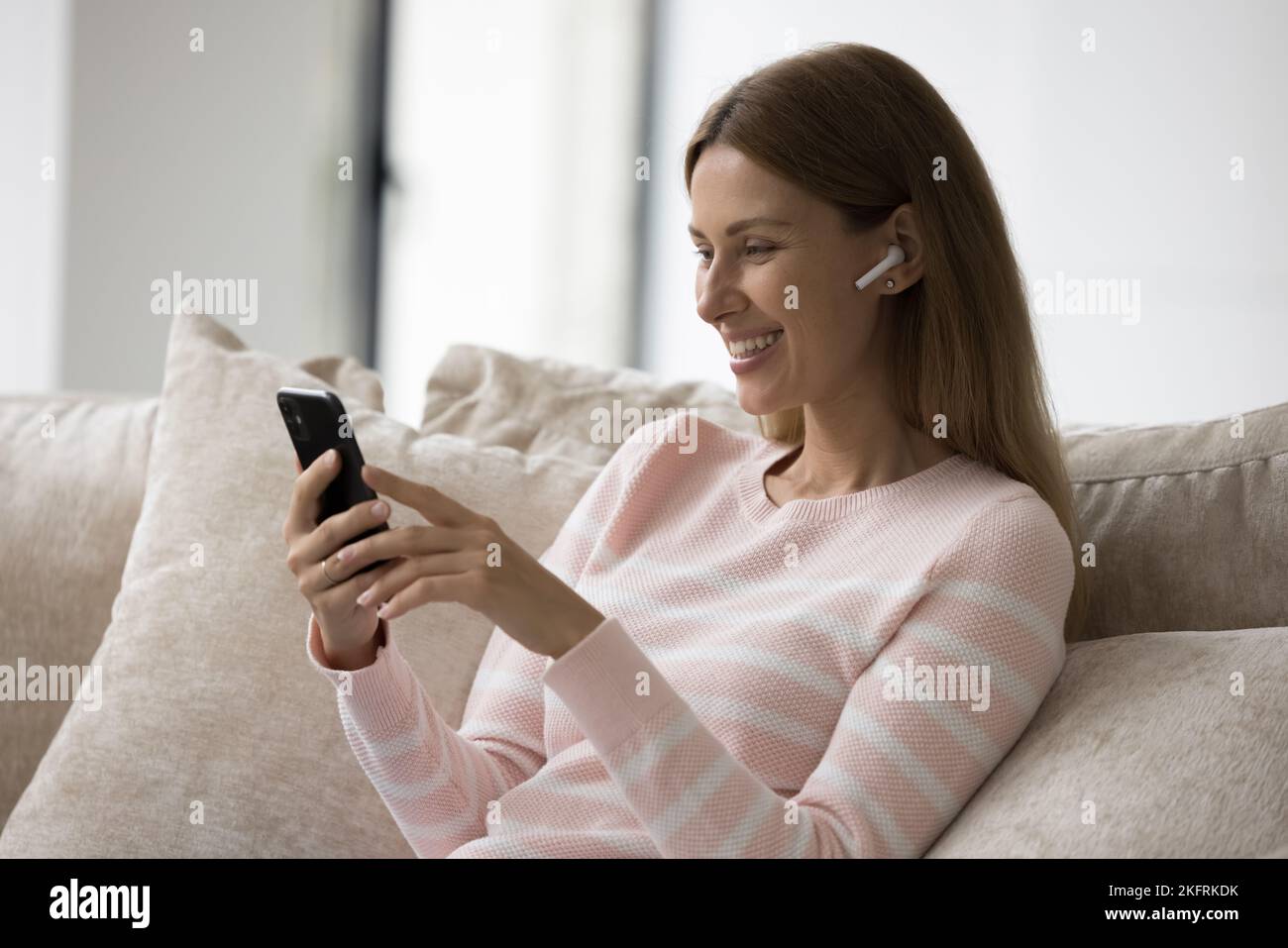 Frau hält das Smartphone und hört Audionachrichten über kabellose Kopfhörer Stockfoto