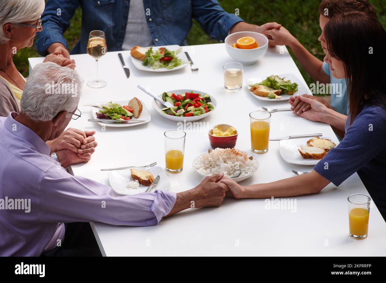 Dankbar für das, was sie essen werden. Eine Familie mit mehreren Generationen, die vor dem gemeinsamen Essen Gnade sagt. Stockfoto