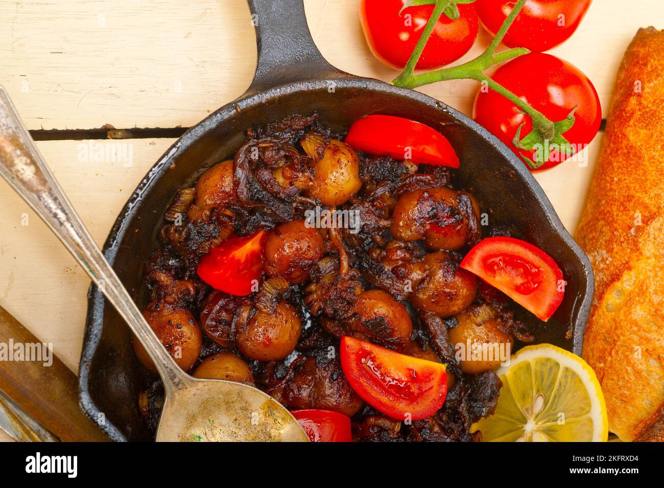 Baby Tintenfisch über rustikalen Holztisch auf eisernen Pfanne mit Tomaten und Zwiebeln gebraten Stockfoto