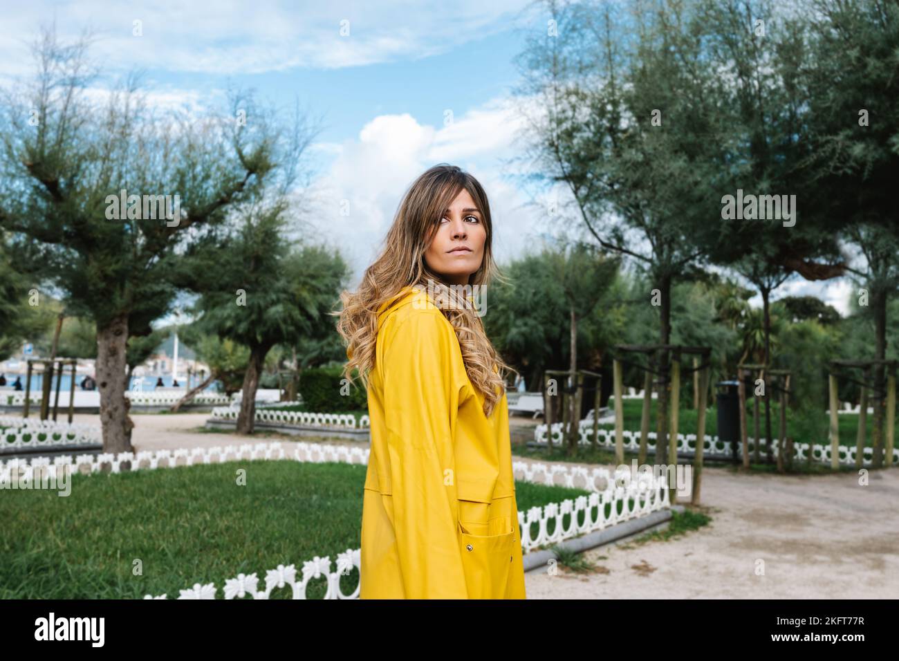 Trendiges Weibchen mit welligen Haaren, das im Park mit grünem Gras und Bäumen in Donostia von San Sebastian in Spanien wegschaut Stockfoto