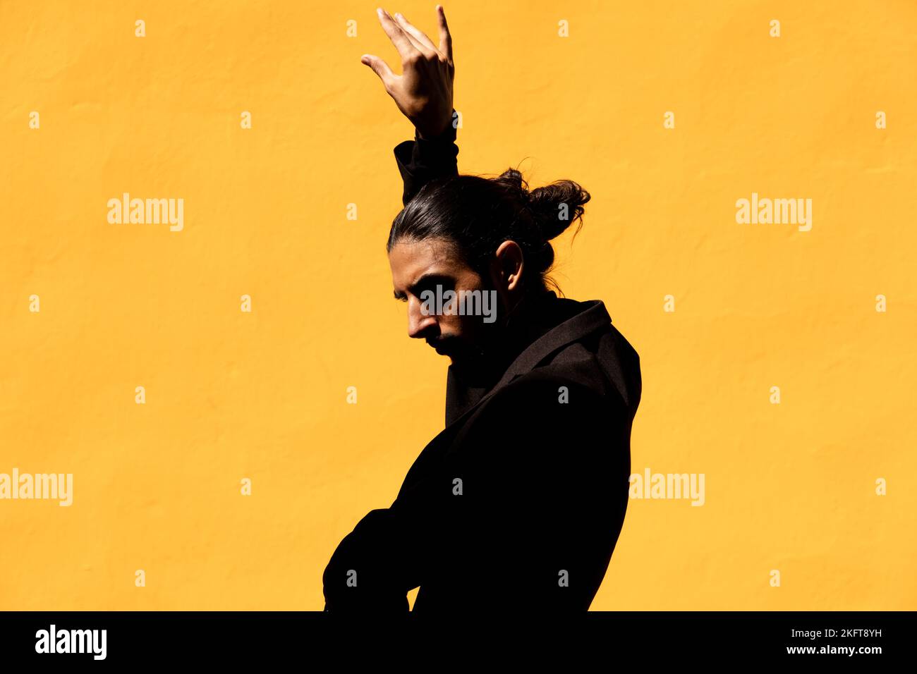 Hispanischer Mann in schwarzem Anzug mit Haarbüsch gestikulierend und tanzend Flamenco gegen gelbe Wand Stockfoto