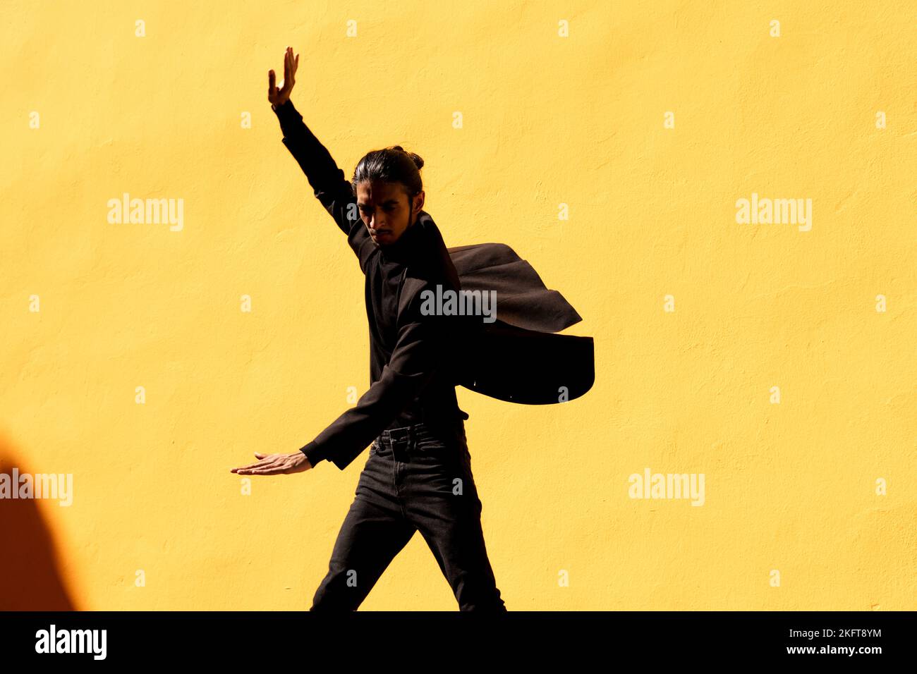 Hispanischer Mann in schwarzem Anzug mit Haarbüsch gestikulierend und tanzend Flamenco gegen gelbe Wand Stockfoto