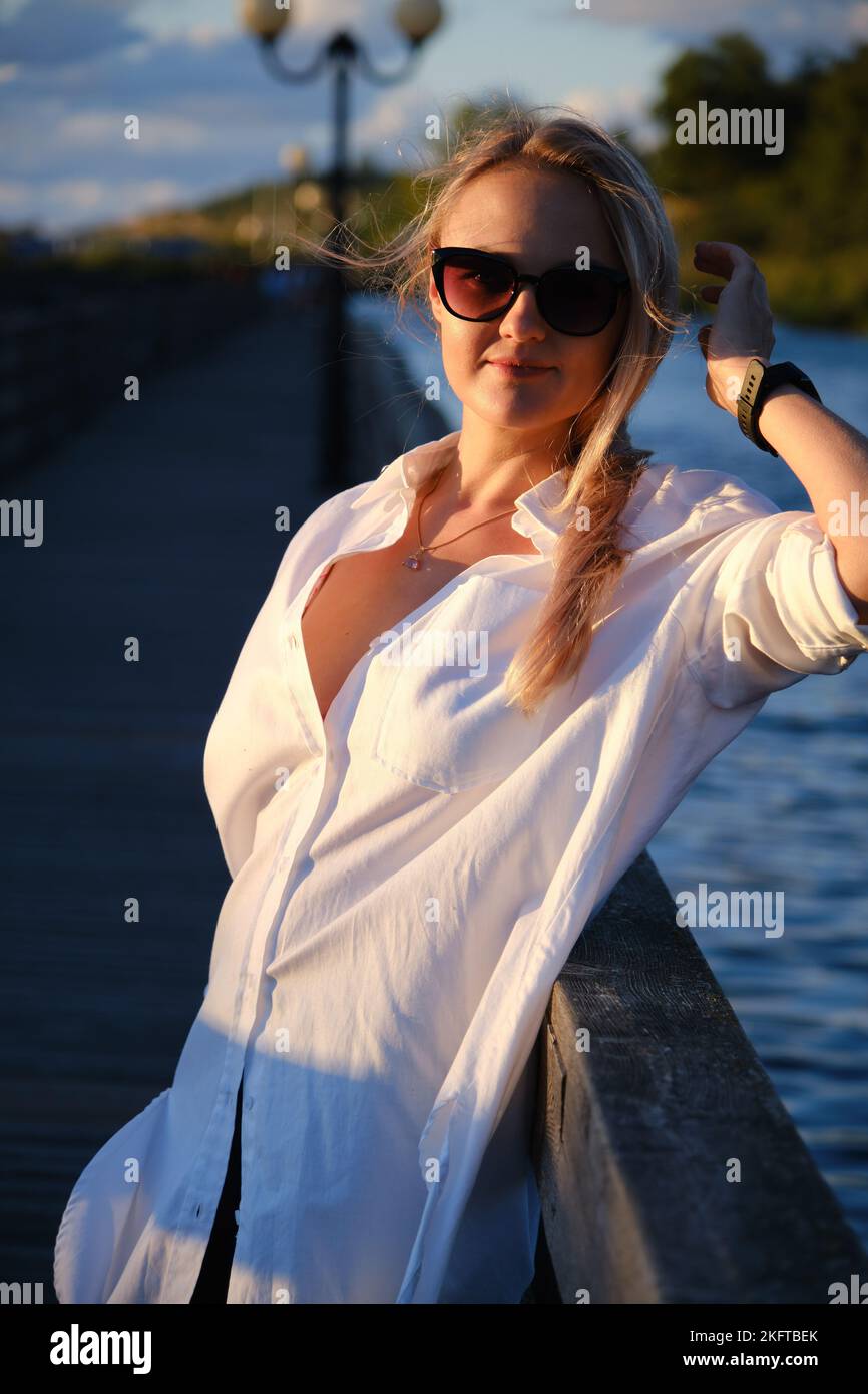 Junge glückliche blonde Frau in Strohhut und Sonnenbrille im Sommer Sonnenuntergang Park Blick auf die Kamera und lächelnd Stockfoto