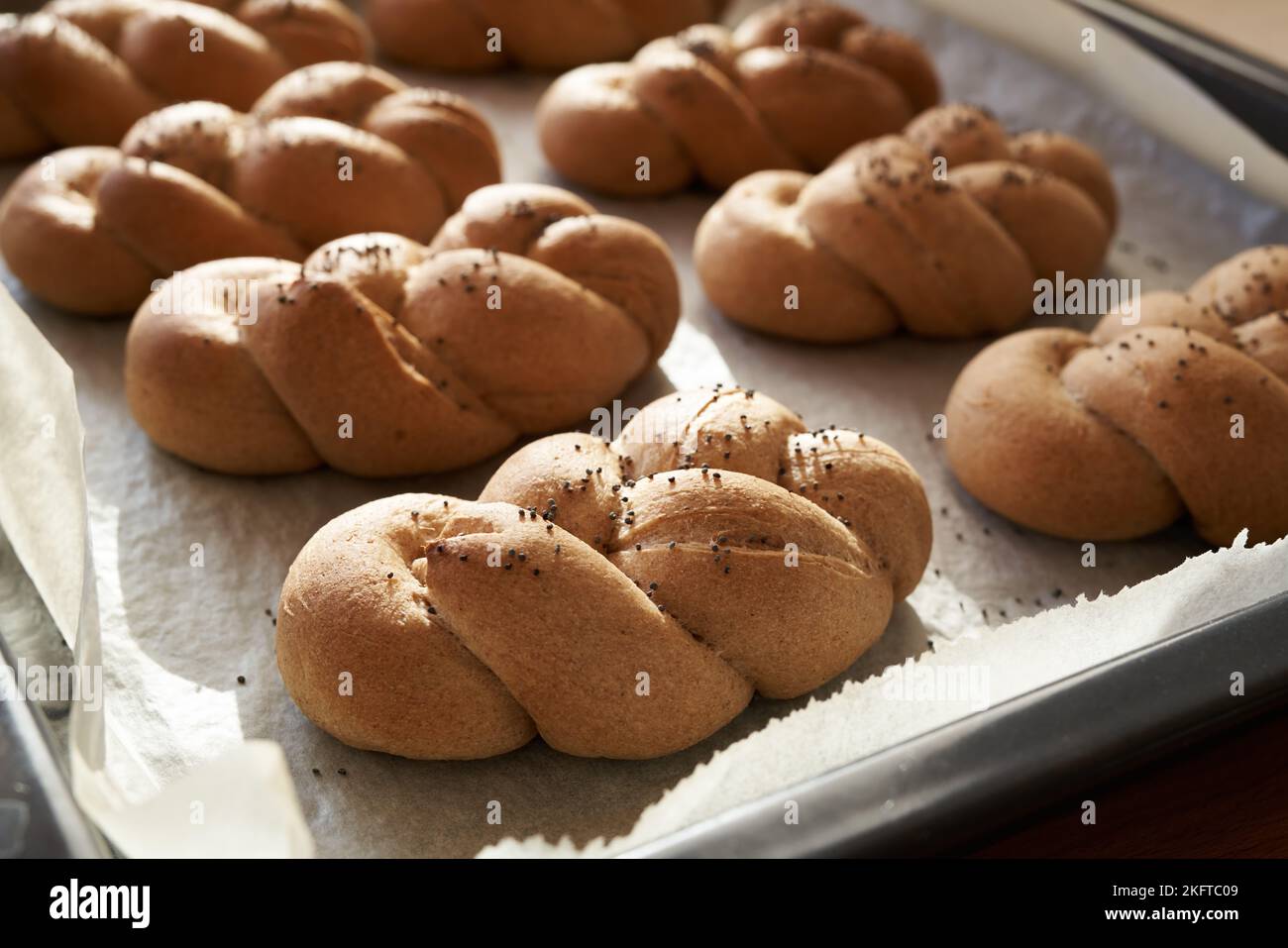 Frisch gebackene geflochtene Brötchen oder Brötchen aus Vollkorn-Dinkelmehl, bestreut mit Mohn Stockfoto