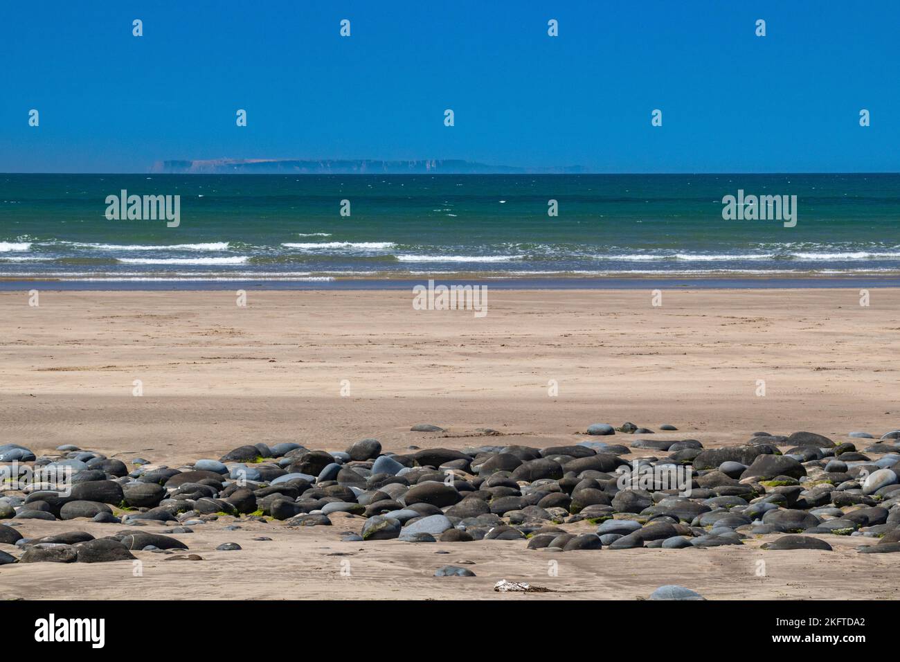 Blick auf den Strand mit Blick auf Kieselsteine und Northam Beach auf den Atlantischen Ozean mit kleinen Wellen und auf die entfernte Lundy Island im Sommer. Stockfoto