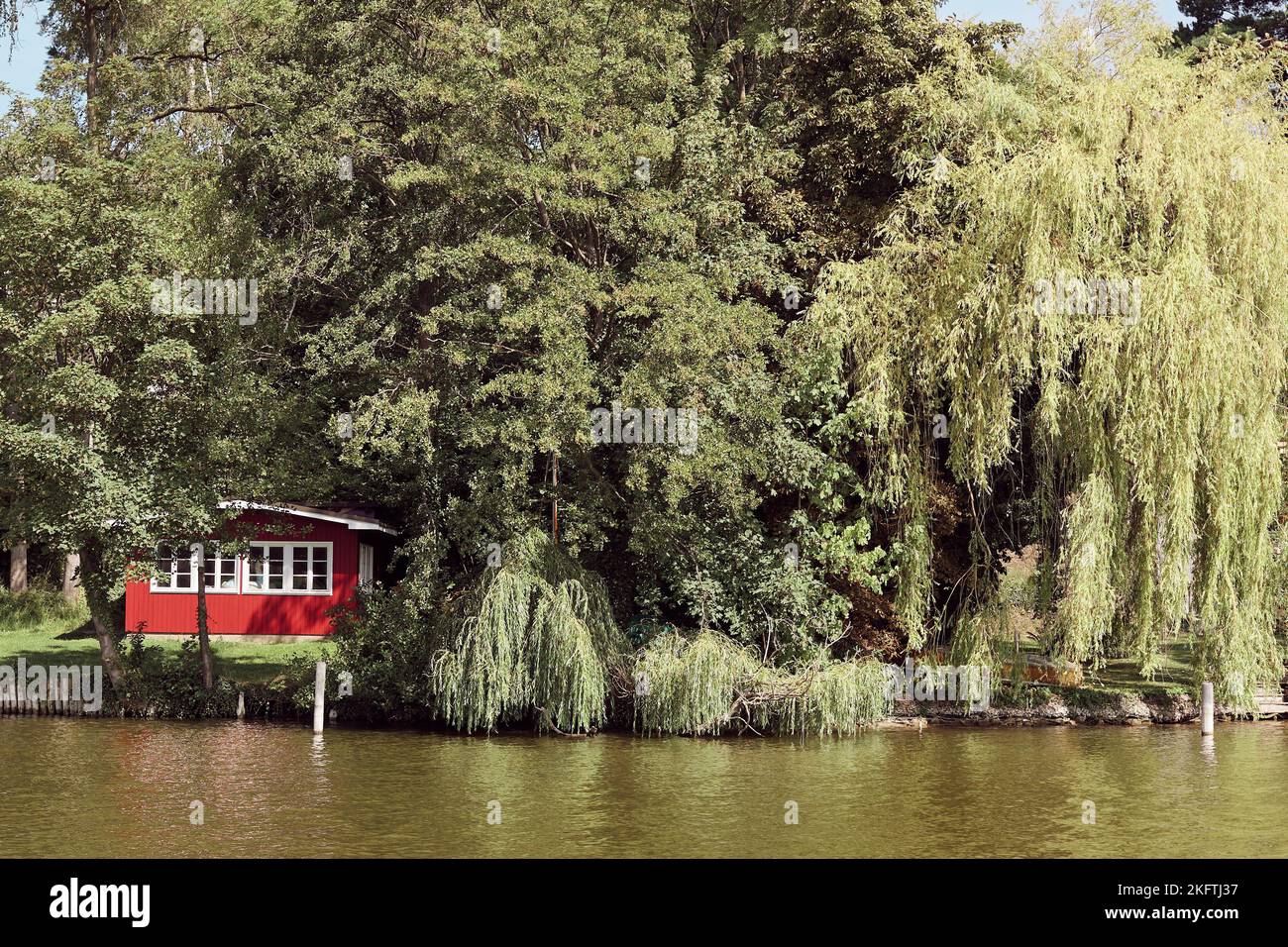 Eine dichte Vegetation und ein rot-ummauertes Haus, das über einen Fluss gesehen wird Stockfoto