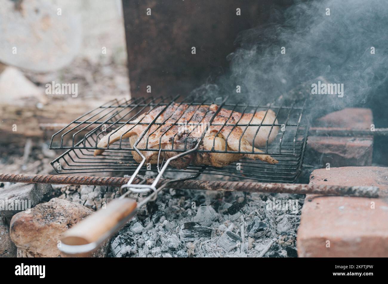 Hühnerfleischfutter werden auf dem Grill auf schwelenden Kohlen oder vom Lagerfeuer auf dem Boden am Sommer- oder Herbsttag gebraten. Grill im Campingzustand Stockfoto