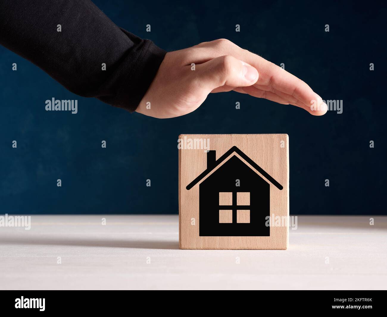 Hausversicherung und Schutzkonzept. Männliche Hand steht schützend über dem Holzblock mit Heimsymbol. Stockfoto Hausversicherung und Schutzkonzept. Männliche Hand steht schützend über dem Holzblock mit Heimsymbol. Stockfoto