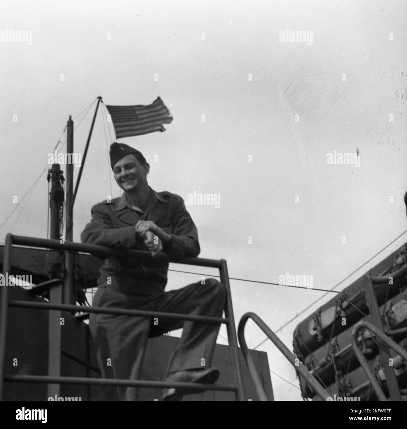 Glücklicher Mann mit amerikanischer Flagge im Hintergrund. Veteranen der United States Army kommen nach dem Zweiten Weltkrieg auf dem Elgin Victory Schiff nach Hause SS Elgin Victory, ein von Permanente Metals gebautes Schiff vom Typ VC2-S-AP2 Victory Stockfoto