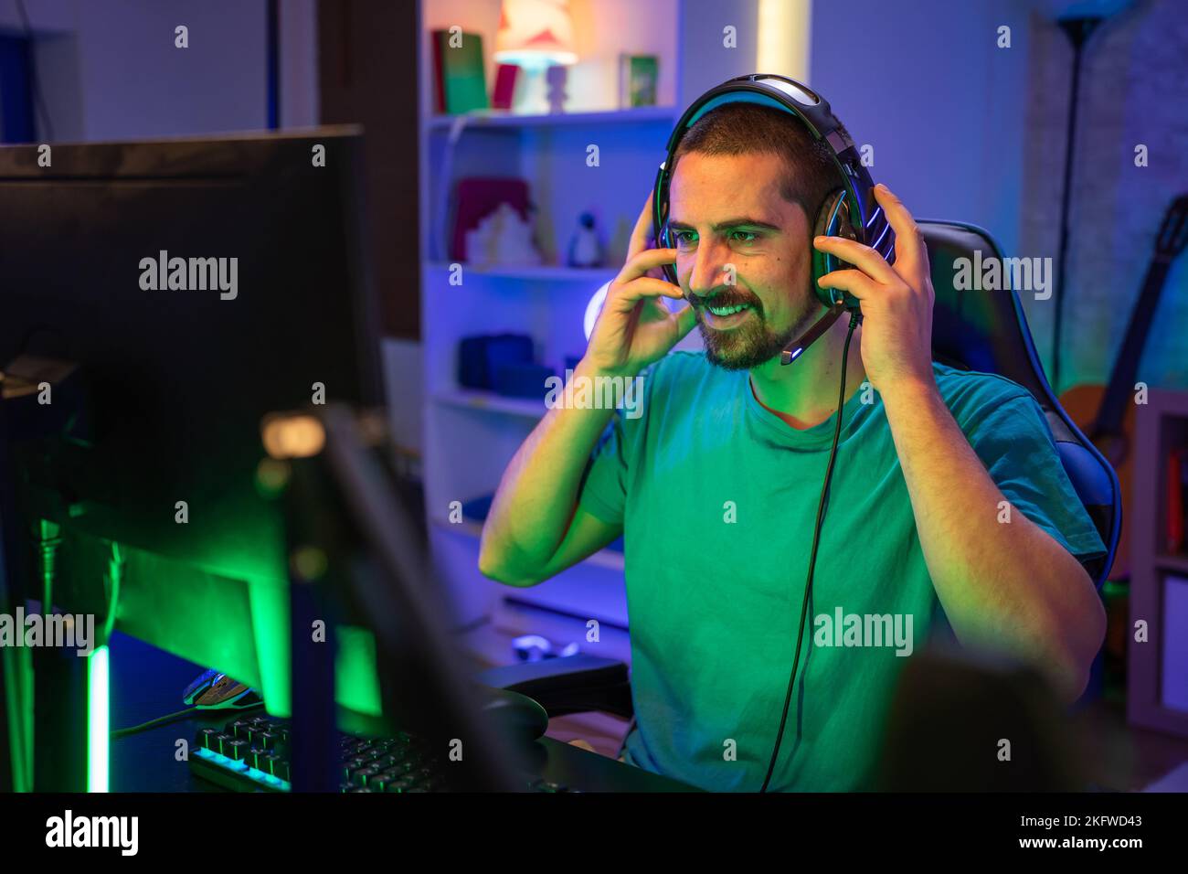 Gamer spielen aufgeregt Online-Videospiel mit Kopfhörern Streaming auf Computer in einem Neonlicht-Raum. Stockfoto
