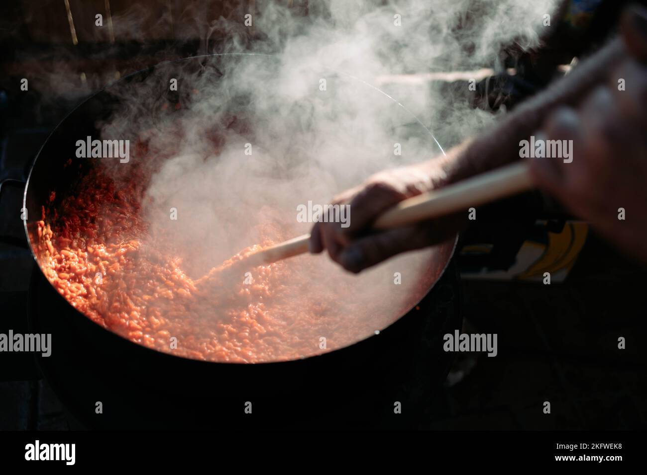 Männliche Hand rührt Ajvar in einem großen Topf. Ajvar, traditionelle Zubereitung von Mahlzeiten Stockfoto