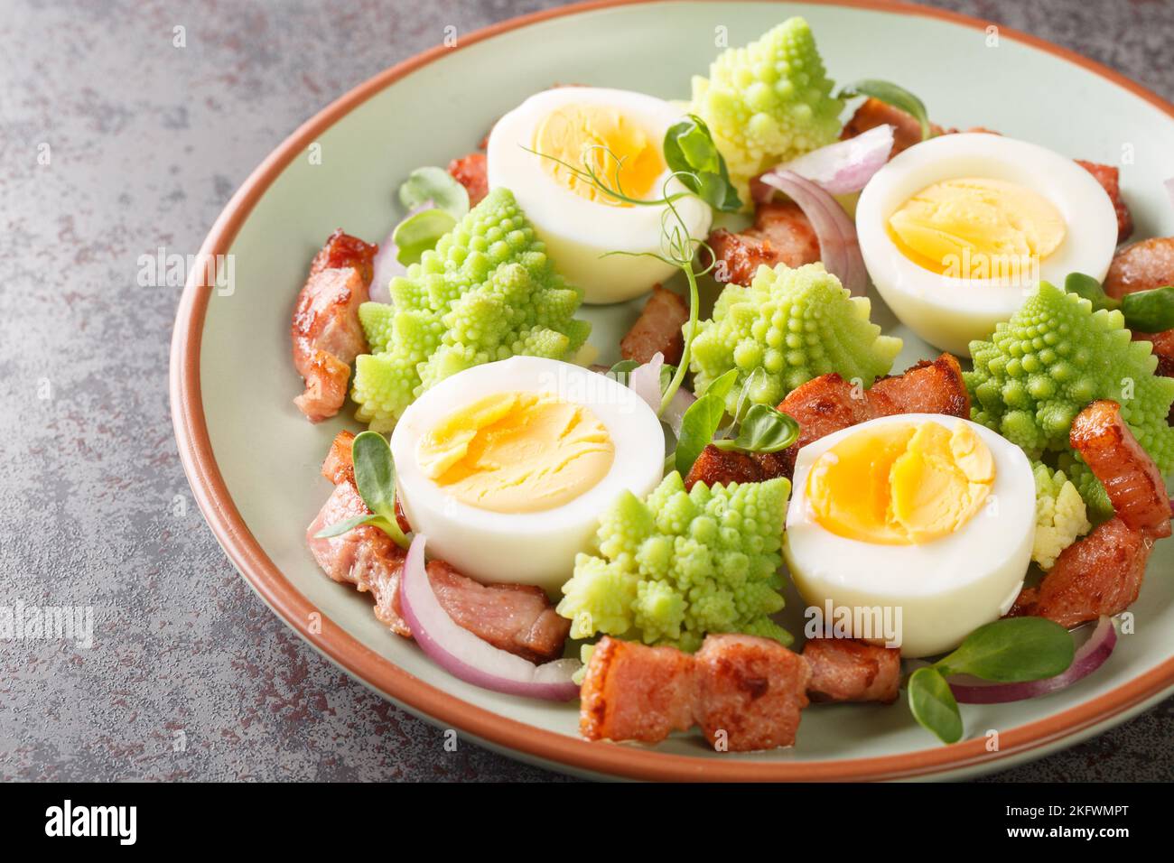 Gedünsteter romanesco-Brokkoli, gekochte Eier, gebratener Speck und frisches Mikrogemüse in Nahaufnahme auf einem Teller auf dem Tisch. Horizontal Stockfoto