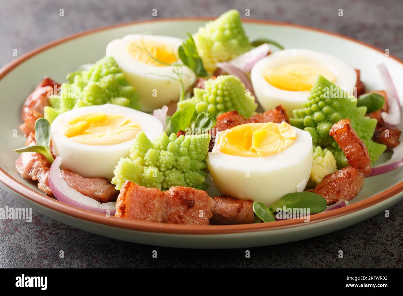Hausgemachter Salat aus gedünstetem Romanesco-Kohl, gekochten Eiern, gebratenem Speck und frischem Mikrogemüse in Nahaufnahme auf einem Teller auf dem Tisch. Horizontal Stockfoto