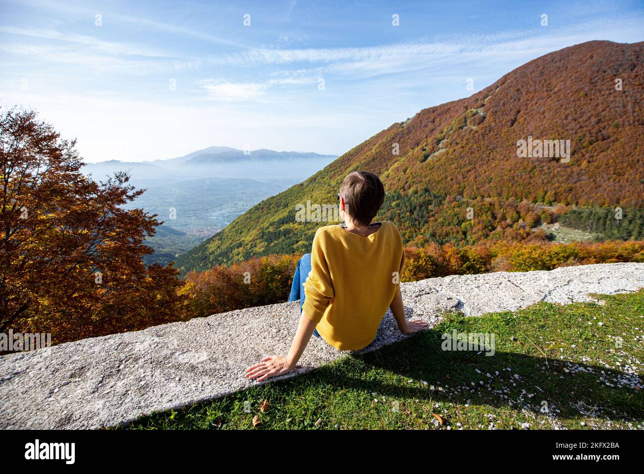 Die junge Frau sitzt und schaut sich die Herbstlandschaft in Italien an. Die Frau sitzt und blickt auf das Tal mit seinen Herbstfarben. Stockfoto