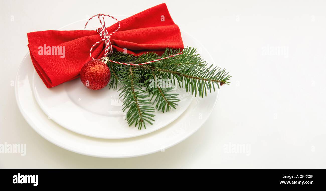 Weihnachtliche Tischkulisse, Festessen. Rote Stoffserviette und Weihnachtsdekoration auf Tellern, weißer Hintergrund Stockfoto