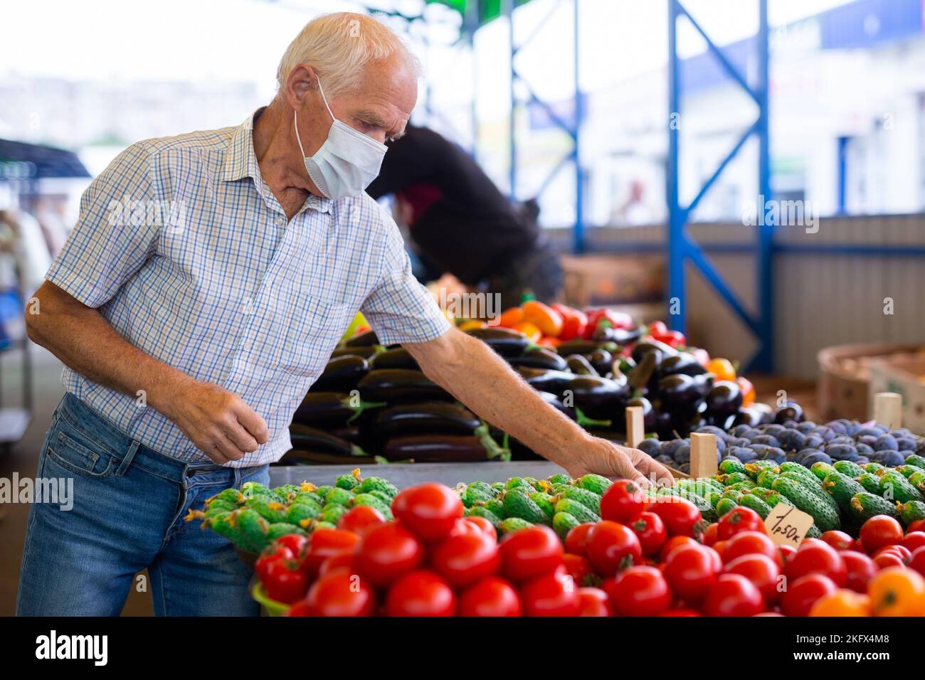 Pensionierter europäischer Mann mit medizinischer Maske zum Schutz vor Viren, der Tomaten auf dem Markt kauft Stockfoto