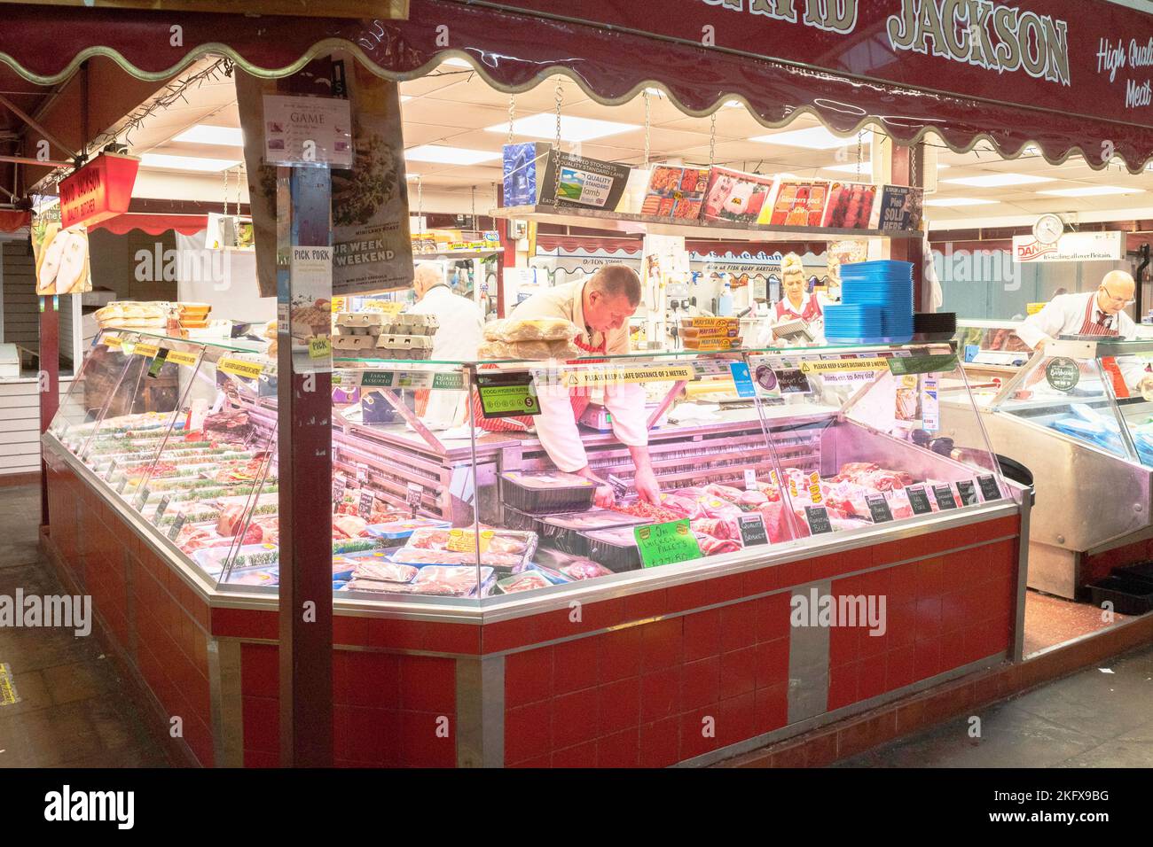 Metzger, der die Ausstellung auf dem Fleisch- und Tortenstand von David Jackson Butchers Ltd in der Markthalle von Darlington aufräumte Stockfoto