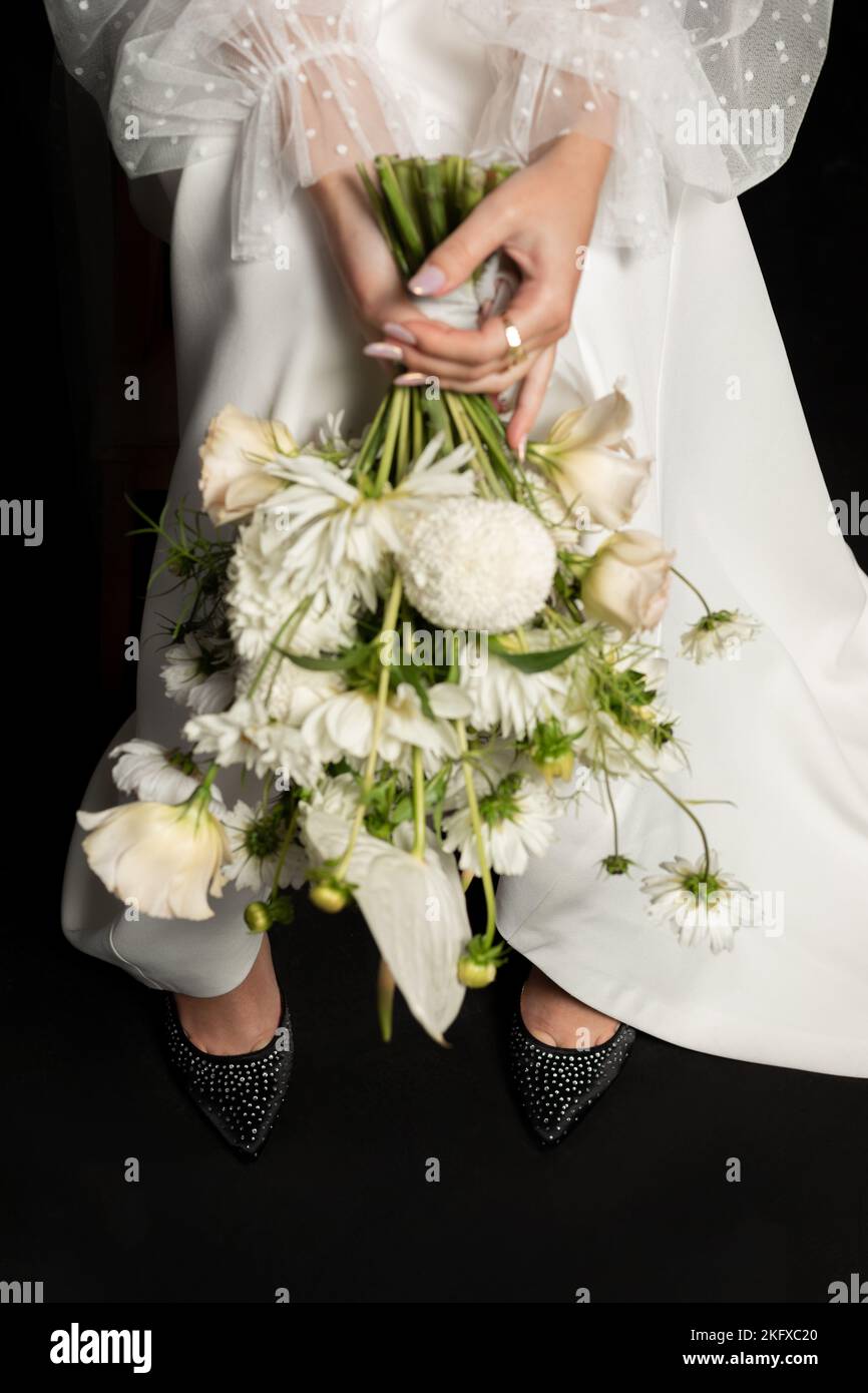 Vertikale unkenntlich Frau sitzen in weißem Kleid halten Blumenstrauß in den Händen mit Maniküre auf schwarzem Hintergrund. Modell Stockfoto