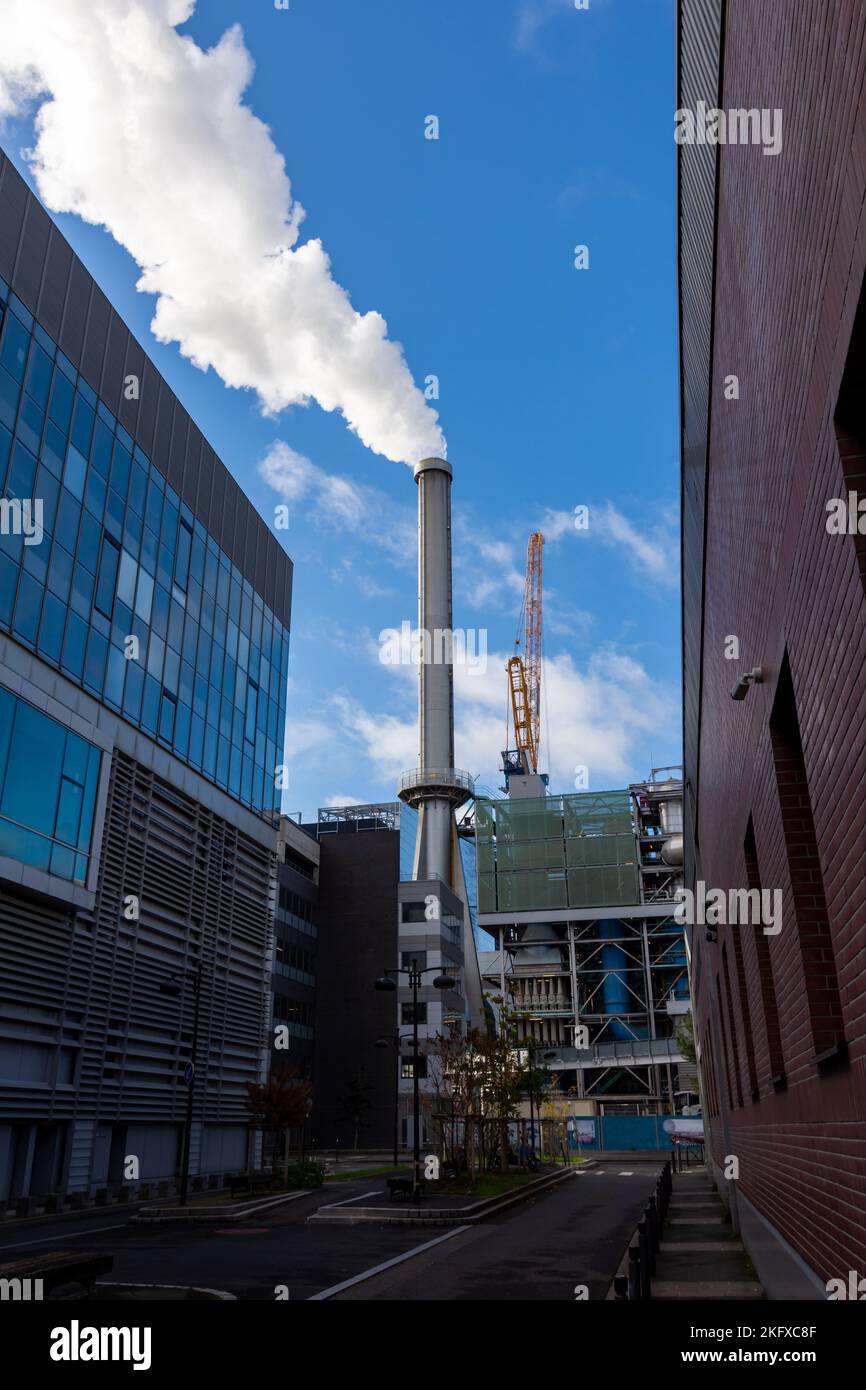 Schornstein einer Fabrik, der dichten weißen Rauch in einer Straße eines Industriegebiets emittiert. Konzepte der Luftverschmutzung, der Stromerzeugung und der CO2-Emissionen Stockfoto