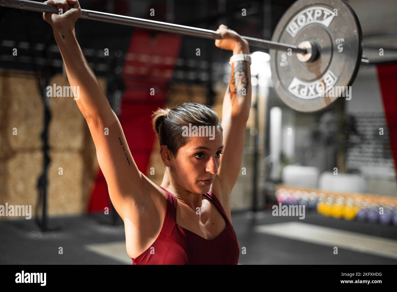 Brunette kaukasische Mädchen mit rotem Top und Tattoos tun Gewichtheben in einem großen Fitnessstudio Stockfoto