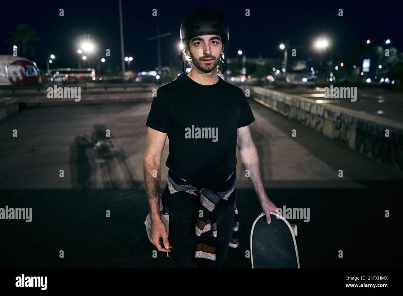 kaukasischer Junge Skater in einem gestreiften Pullover an der Taille gebunden hält ein Skateboard mit seiner Hand in der Stadt Nacht Stockfoto