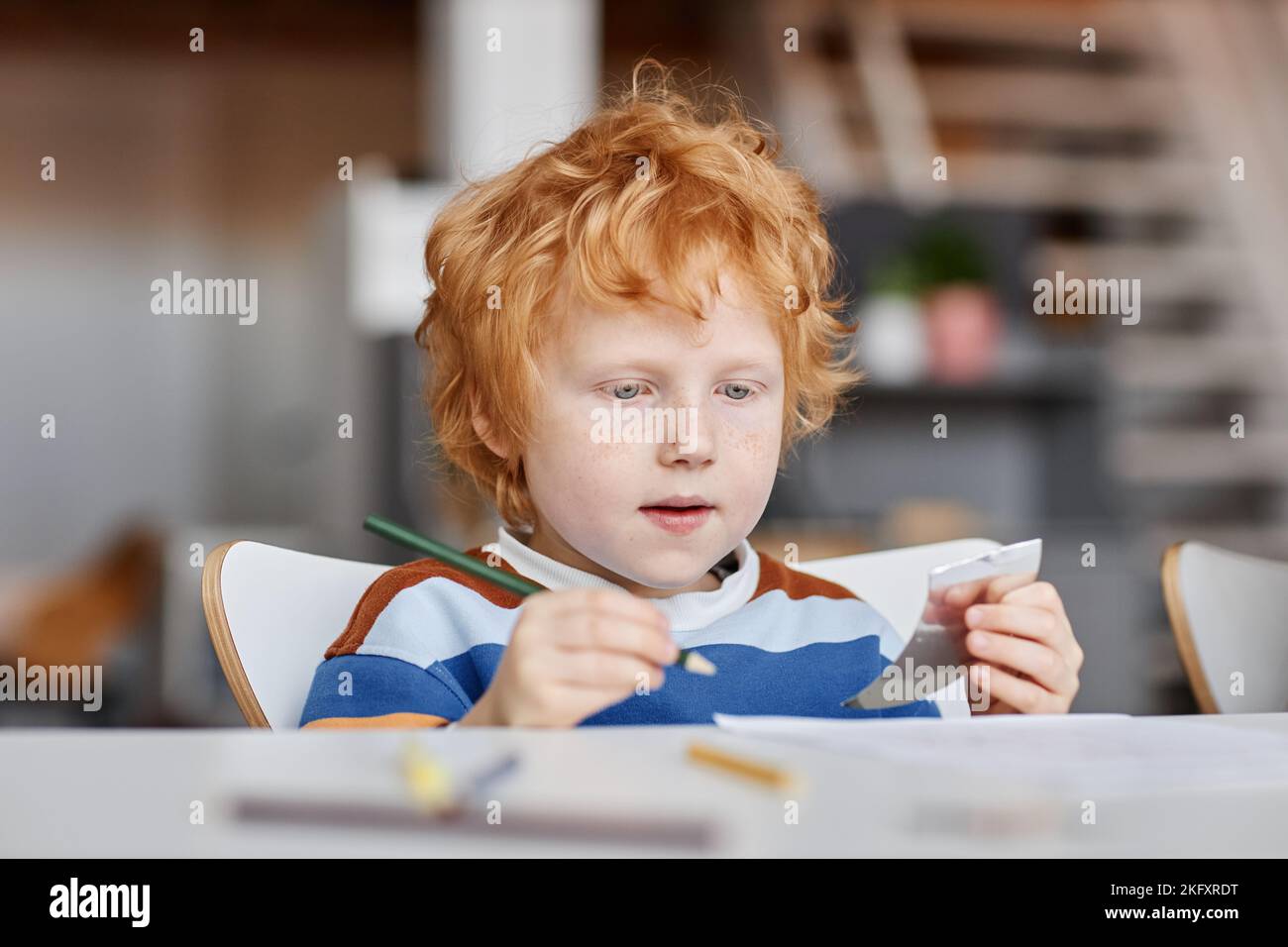 Nette fleißige kingerhaarige Lerner der Kindergarten mit Buntstift der dunkelgrünen Farbe Zeichnung am Schreibtisch bei der Lektion während der individuellen Arbeit Stockfoto