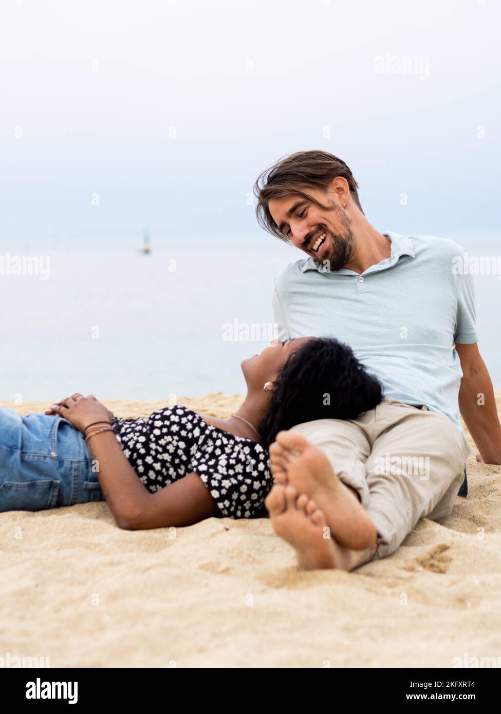 Heterosexuell vielfältiges junges Paar, das liebevoll vor dem Meer sitzt Stockfoto