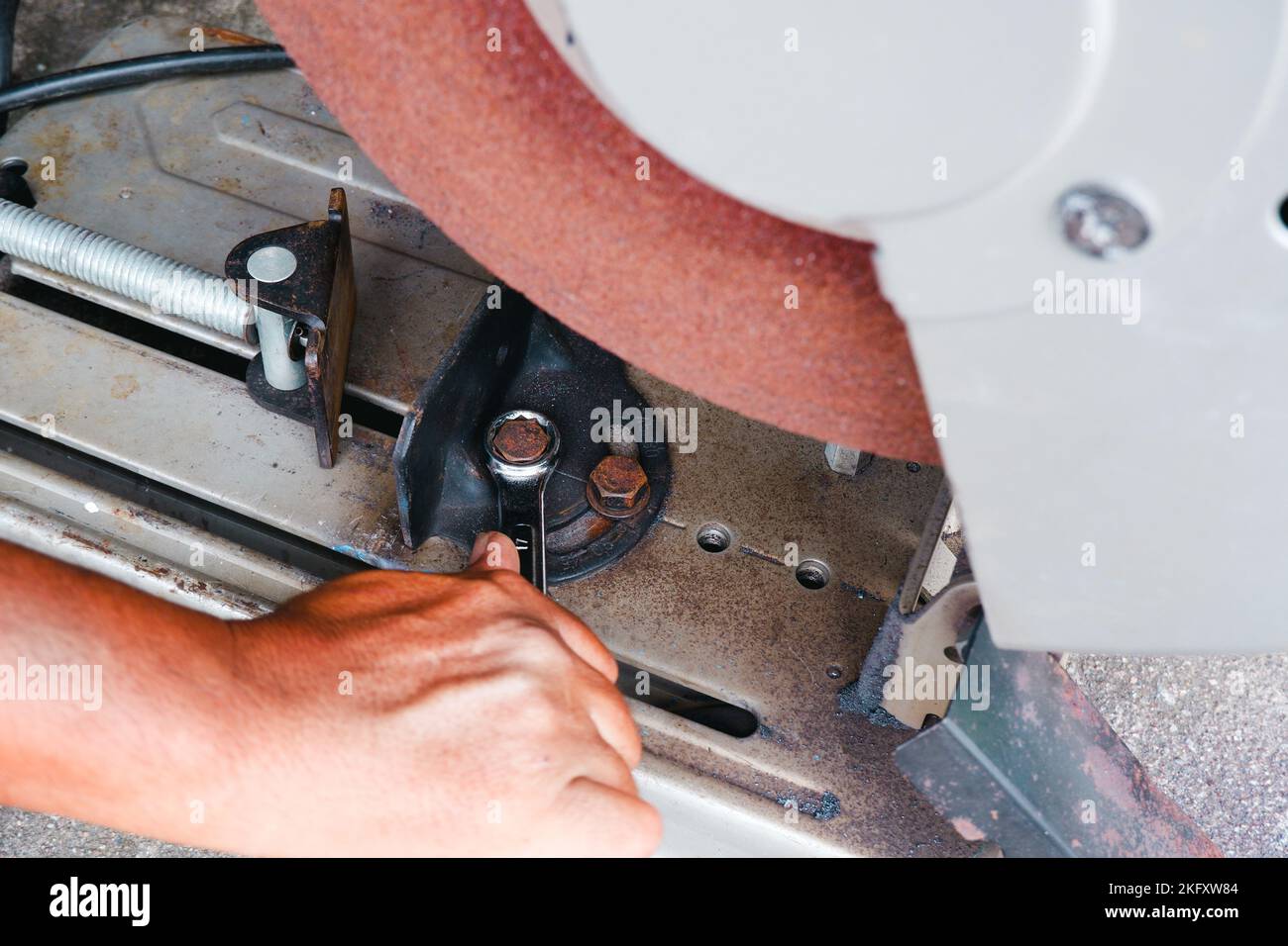 Der Techniker zieht die Mutter an, um den Schnittwinkel der abgeschnittenen Säge mit einem Gabelschlüssel einzustellen Stockfoto