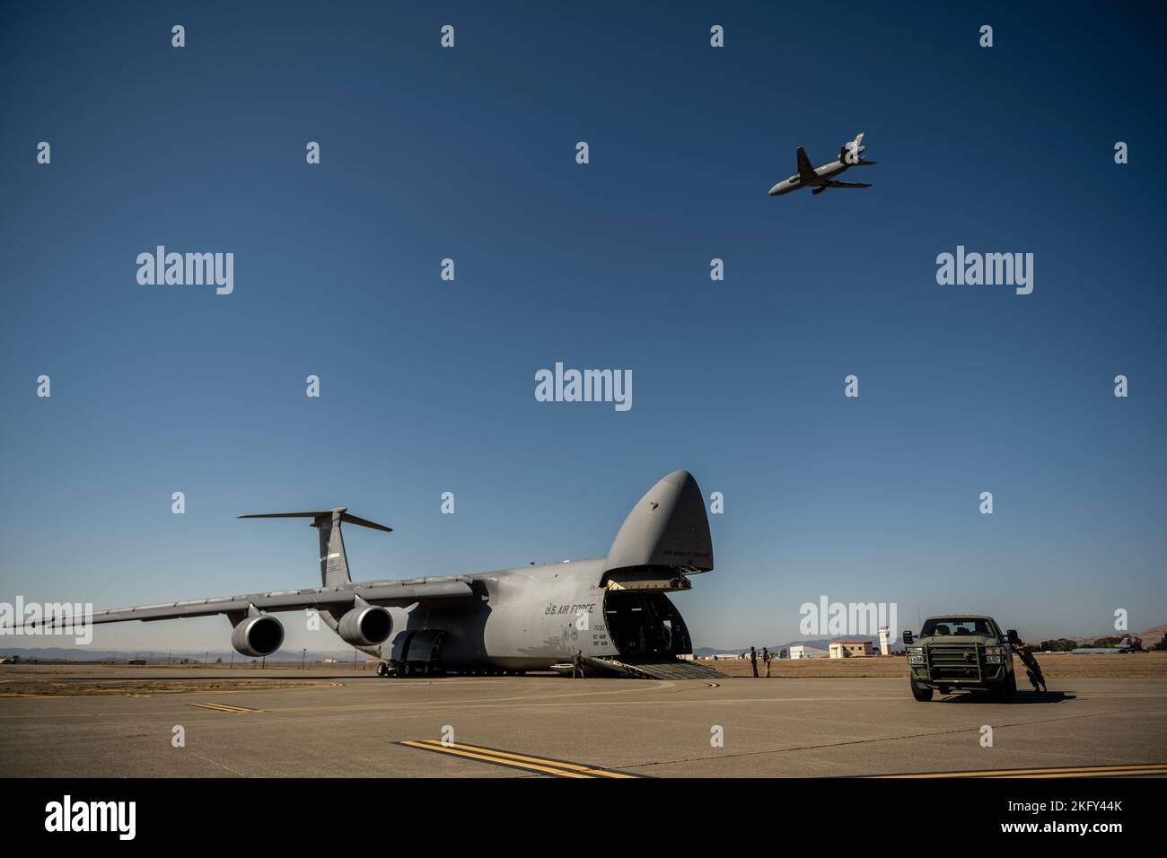 U.S. Airmen, die dem 921. Kontingenzreaktionsgeschwader zugewiesen sind, führen eine Entladung von einer C-5M Super Galaxy aus, da die Motoren laufen, während ein KC-10 Extender während der Übung Dragon Spark auf der Travis Air Force Base, Kalifornien, am 14. Oktober 2022 über dem Kopf fliegt. Übung Dragon Spark bot Einheiten des 60. Air Mobility Wings und des 621. Contingency Response Wings die Möglichkeit, Operationen in Vorbereitung auf eine nationale Katastrophe zu synchronisieren. Stockfoto