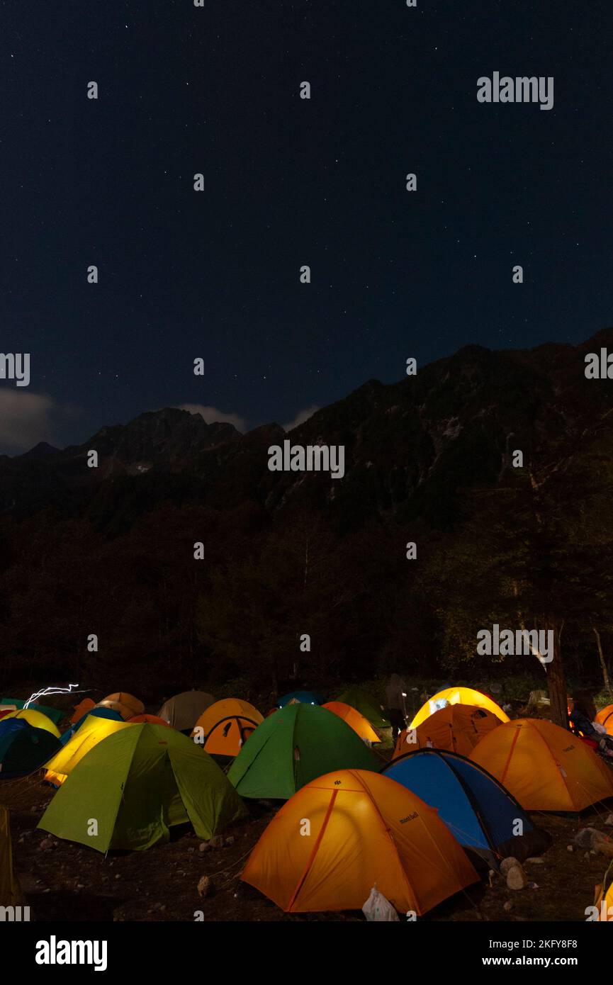 Nachts, unter den Gipfeln der japanischen Alpen, erleuchteten Zelte an einem geschäftigen Wochenende auf dem Tokusawa-Campingplatz in Kamikochi, Japan. Stockfoto