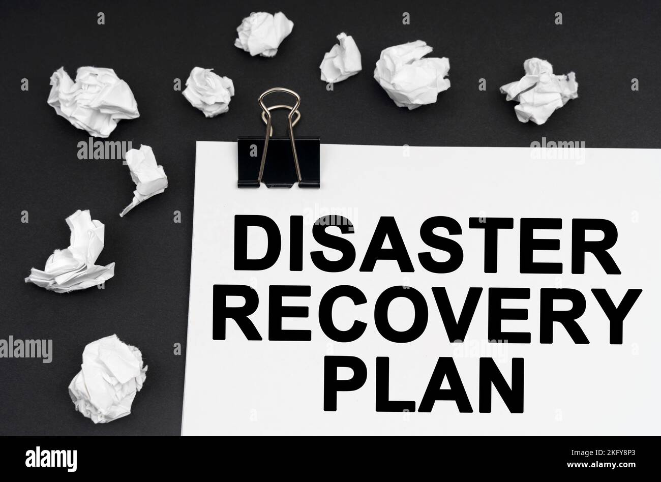 Industriekonzept. Auf schwarzem Hintergrund befinden sich zerknitterte Papierstücke und Papier mit der Aufschrift „Disaster Recovery Plan“ Stockfoto