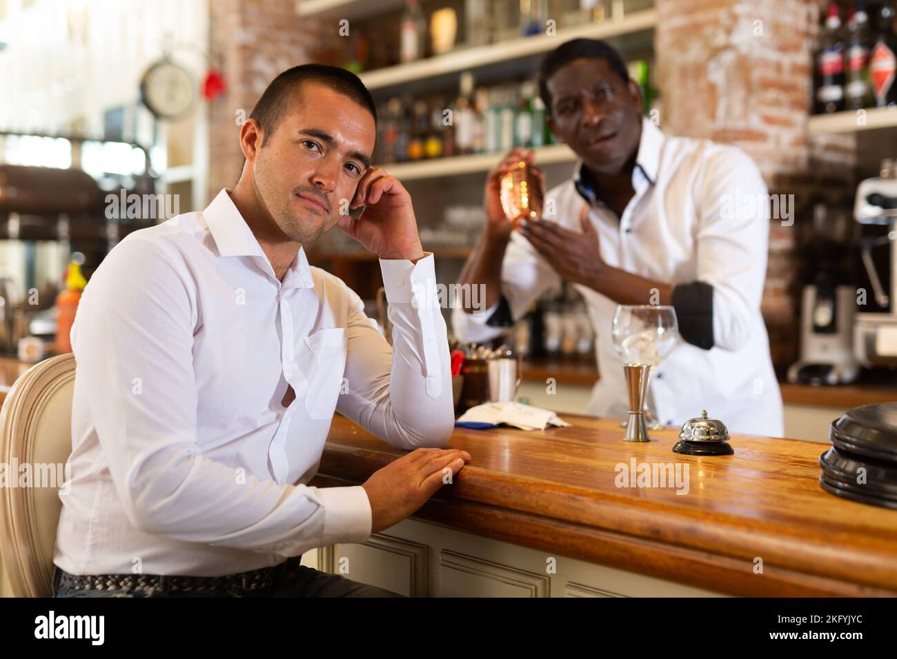 Porträt eines attraktiven Mannes an der Bar. Im Hintergrund bereitet der Barkeeper einen Cocktail zu Stockfoto