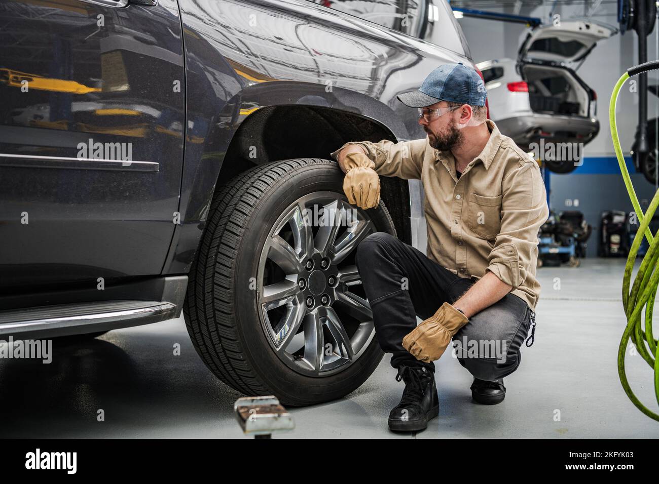 Professioneller Mechaniker mittleren Alters überprüft den Zustand der Autoreifen vor planmäßigen saisonalen Änderungen. Fahrzeugwerkstatt im Hintergrund. Stockfoto