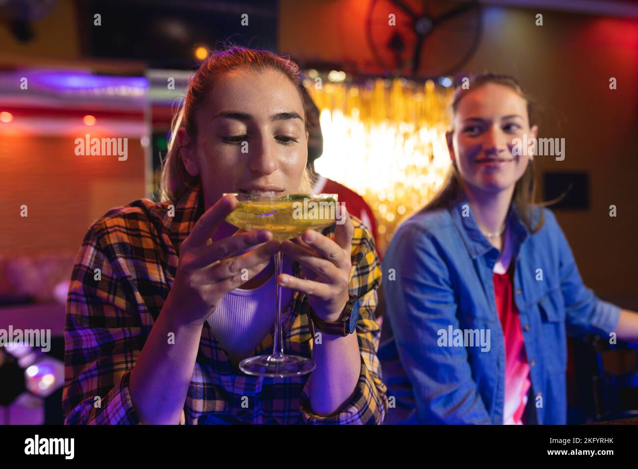 Zwei fröhliche weiße Freundinnen in einer Bar, einer genießt einen Cocktail Stockfoto