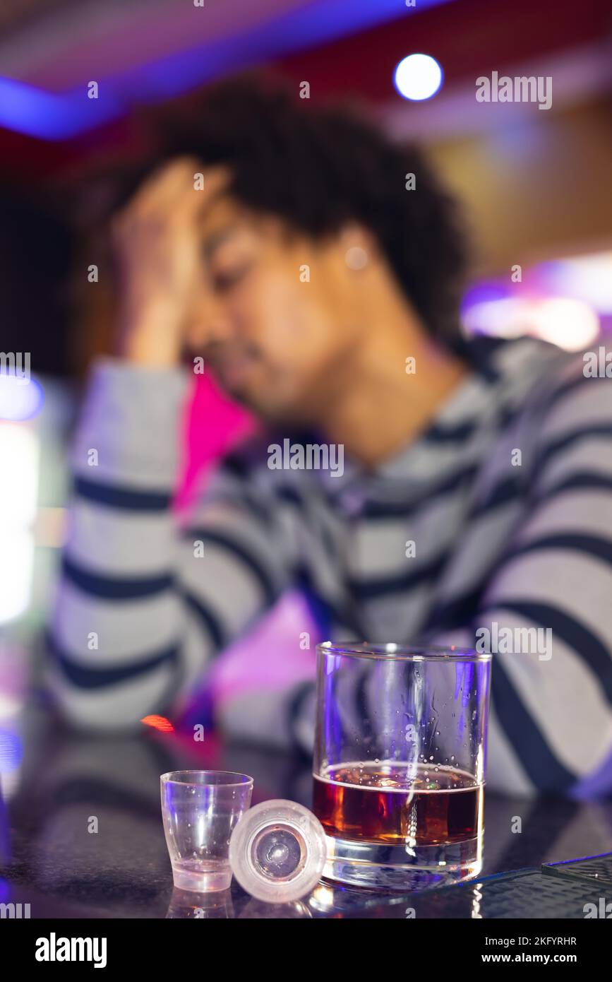Vertikal eines betrunkenen afroamerikanischen Mannes, der Kopf an der Bar hält, Gläser im Vordergrund, selektiver Fokus Stockfoto
