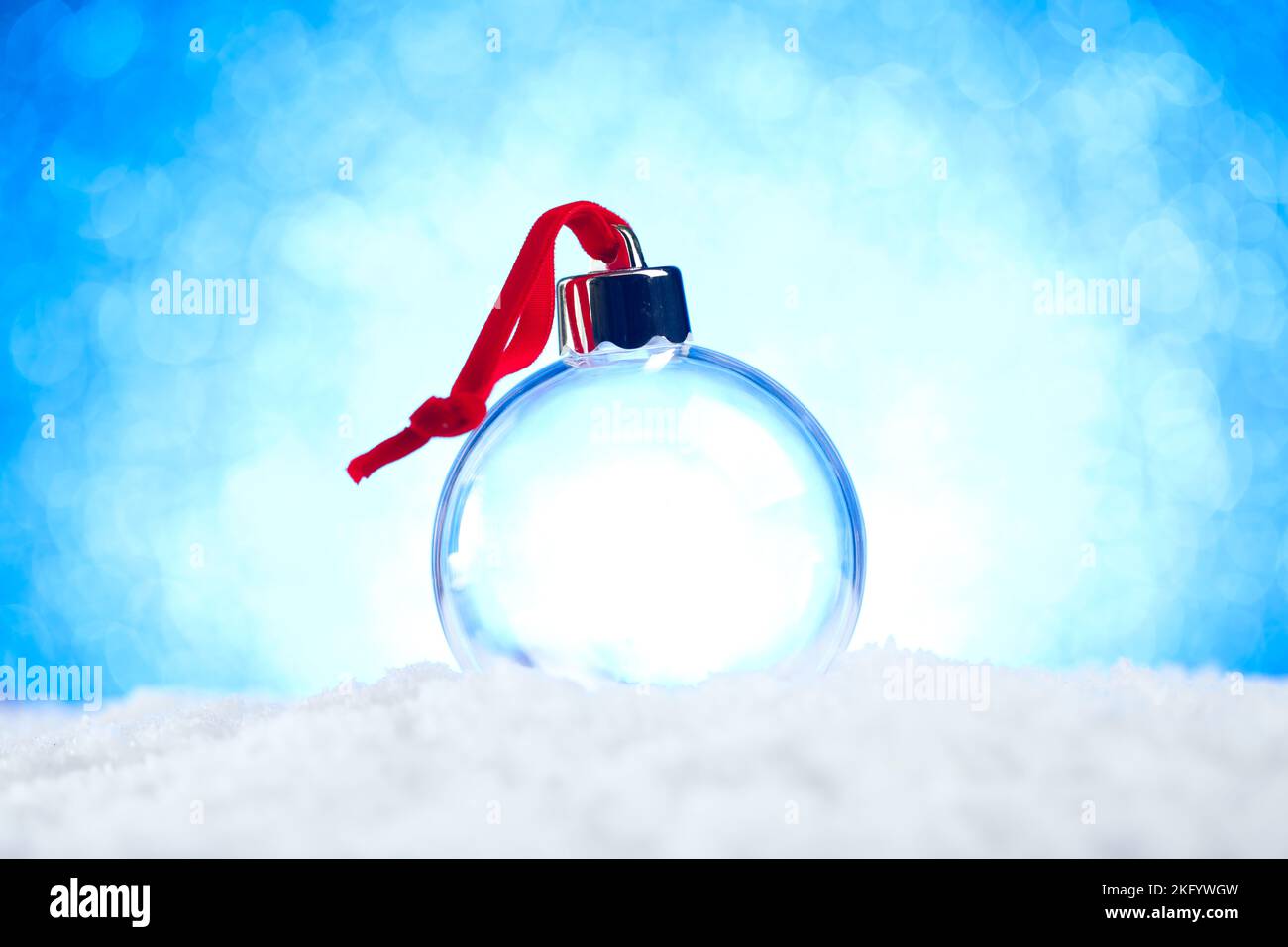 Klare leere Weihnachtsschmuck mit rotem Band sitzt im Schnee mit glänzend blauen Lichter Bokeh Hintergrund Stockfoto