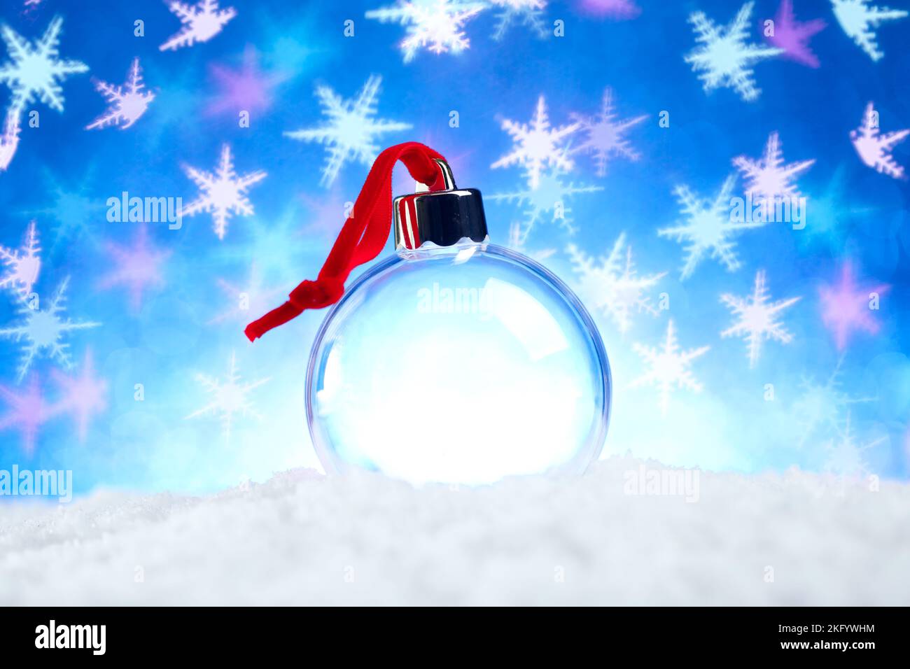 Klare leere Weihnachtsschmuck mit rotem Band sitzt im Schnee mit glänzenden blauen Lichter Schneeflocke Bokeh Hintergrund Stockfoto
