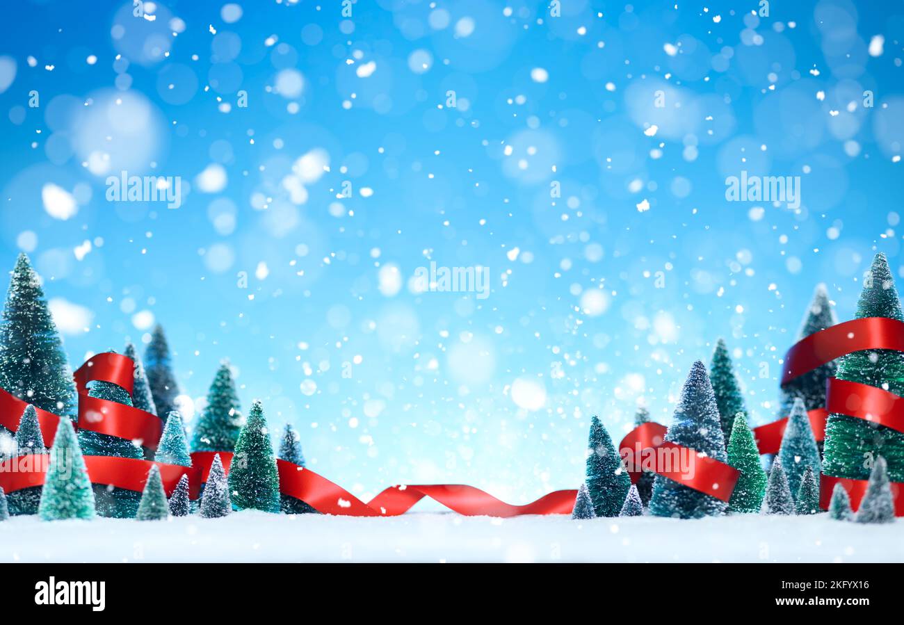 Schneite Winterwunderland mit Miniatur-Baumschmuck in einem glänzenden roten Band auf glitzerndem Schnee gewickelt. Stockfoto