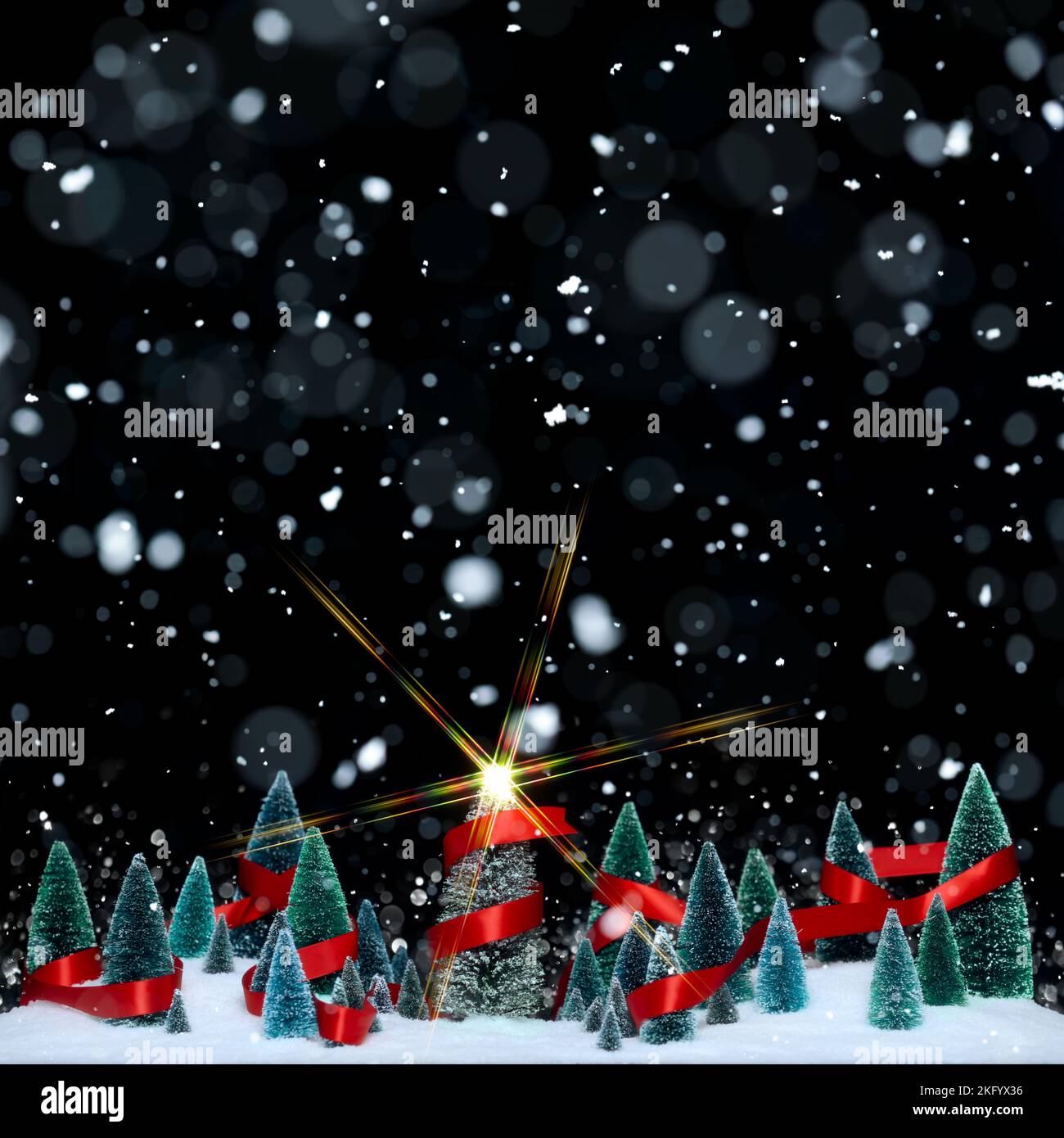 Schneit Winterwunderland mit Miniatur-Baumschmuck in einem glänzenden roten Band mit funkelnden Stern auf Weihnachtsbaum eingewickelt. Stockfoto