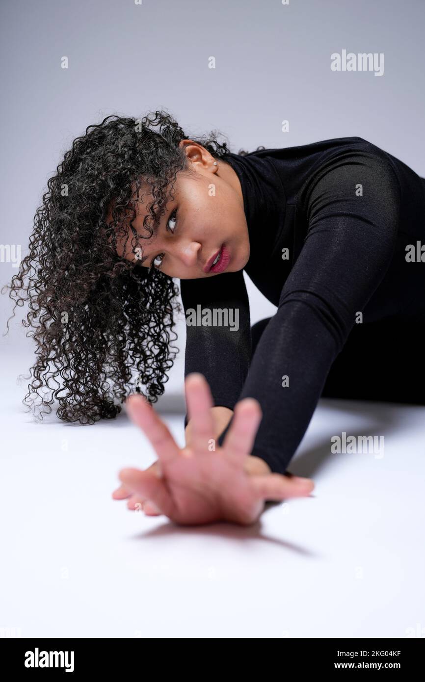 Junge multirassische Frau, die auf dem Boden liegt und in Richtung Kamera reicht | Weißer Hintergrund | intensiver Blick Stockfoto