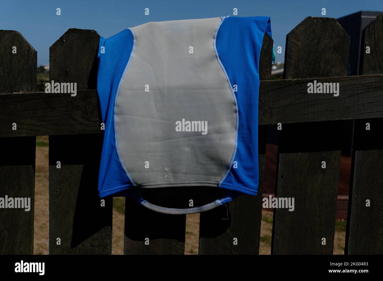 Ein blau-graues Hemd wurde zum Trocknen über einen Zaun geschleudert. Stockfoto