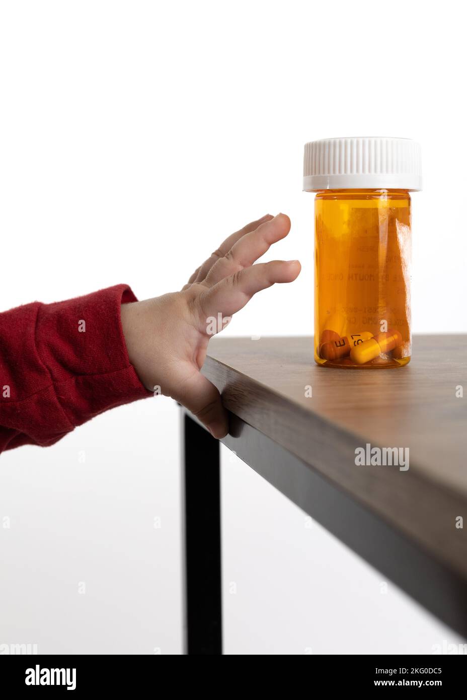 Hände eines Babys, das versucht, eine Flasche Pillen zu erreichen, die auf einem Regal zugänglich ist. Stockfoto