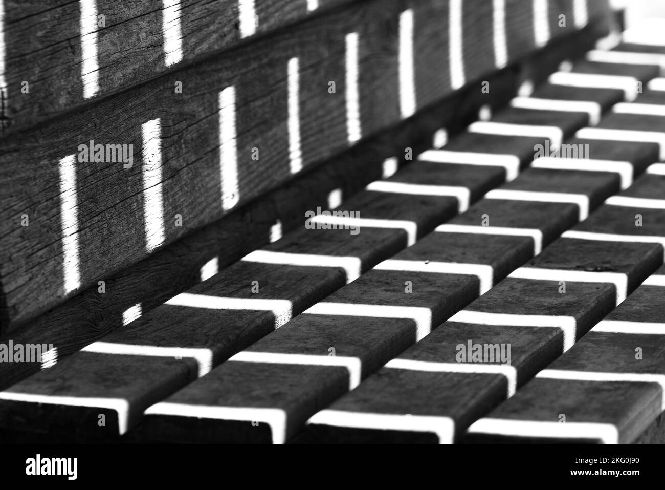 Kontrastreiche Schwarz-Weiß-Fotos des Sonnenlichts, die Muster auf einer Bank bilden Stockfoto