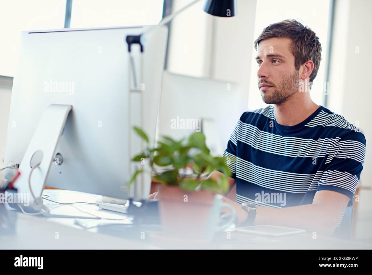 Suche nach digitalen Lösungen. Ein lässig gekleideter junger Mann bei der Arbeit am Computer. Stockfoto