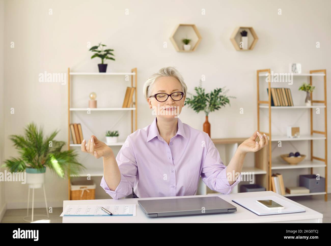 Reife Geschäftsfrau, die eine entspannende Pause bei der Arbeit hat, am Schreibtisch sitzt und meditiert Stockfoto