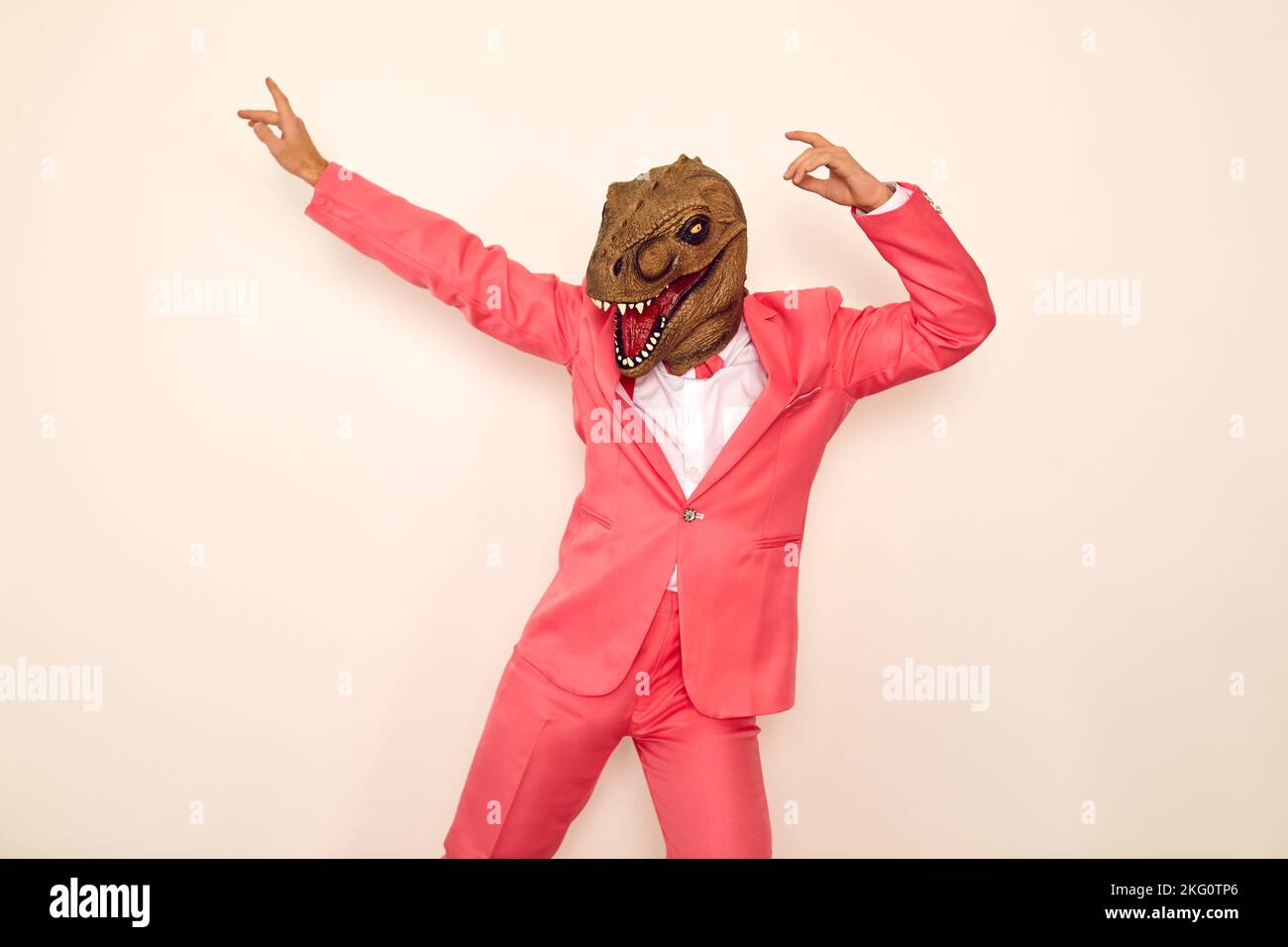 Verrückter junger Mann mit rosa Anzug und lustige Dinosaurier Maske tanzen und Spaß auf der Party Stockfoto