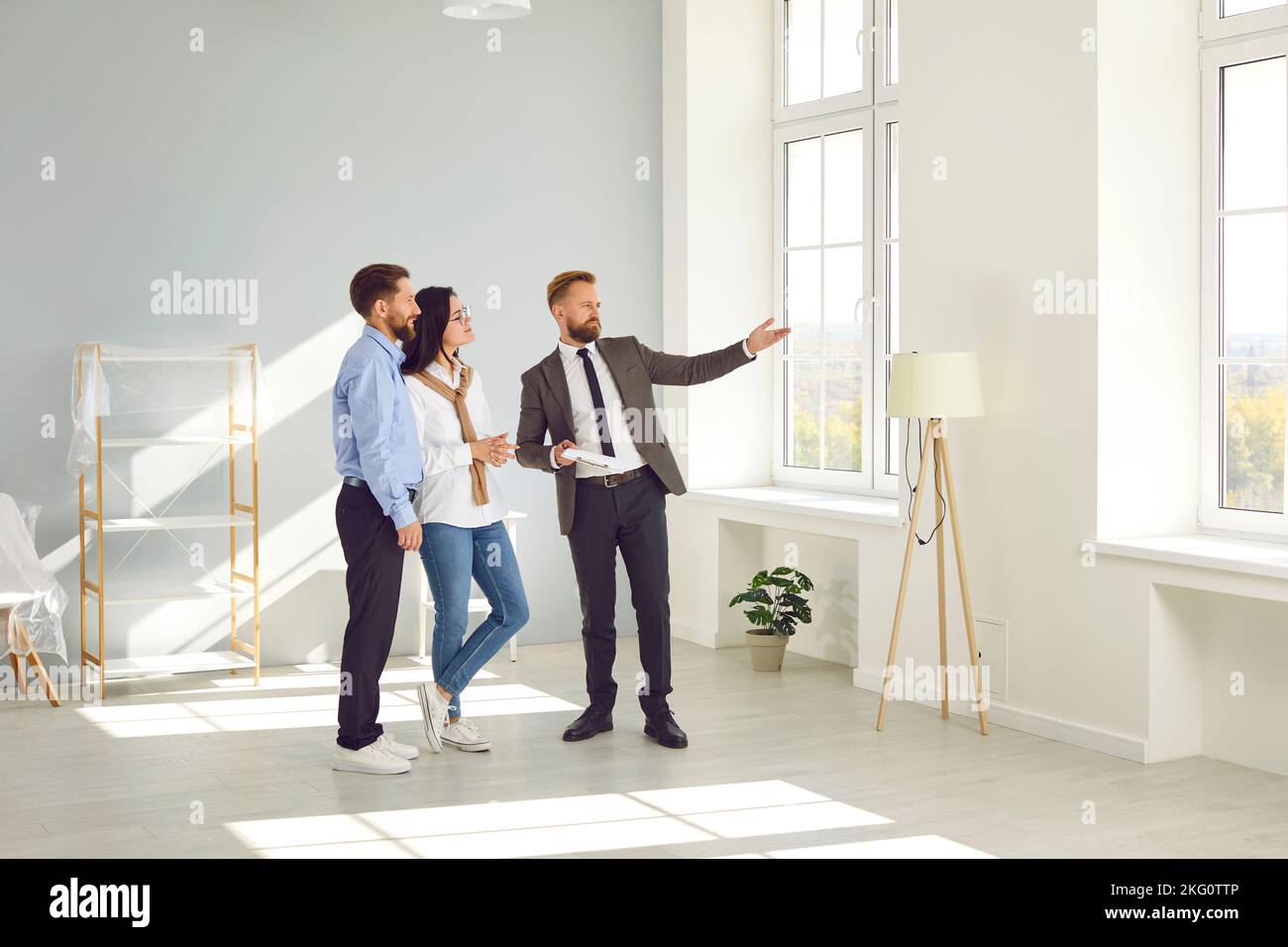 Immobilienmakler junger Mann zeigt neue große moderne Wohnung für ein paar Käufer oder Mieter. Stockfoto