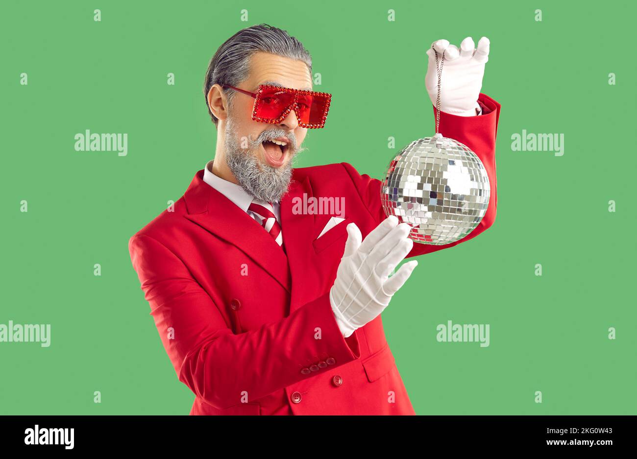 Extravaganter, lächelnder junger Mann in einem roten Anzug und weißen Handschuhen hält einen glänzenden Ball. Stockfoto
