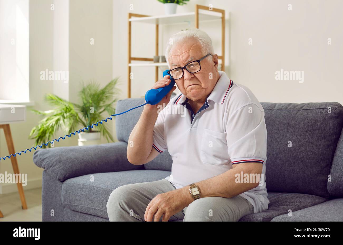 Ein älterer Mann hält fälschlicherweise einen Festnetzhörer und versteht nicht, warum er nichts hören kann. Stockfoto
